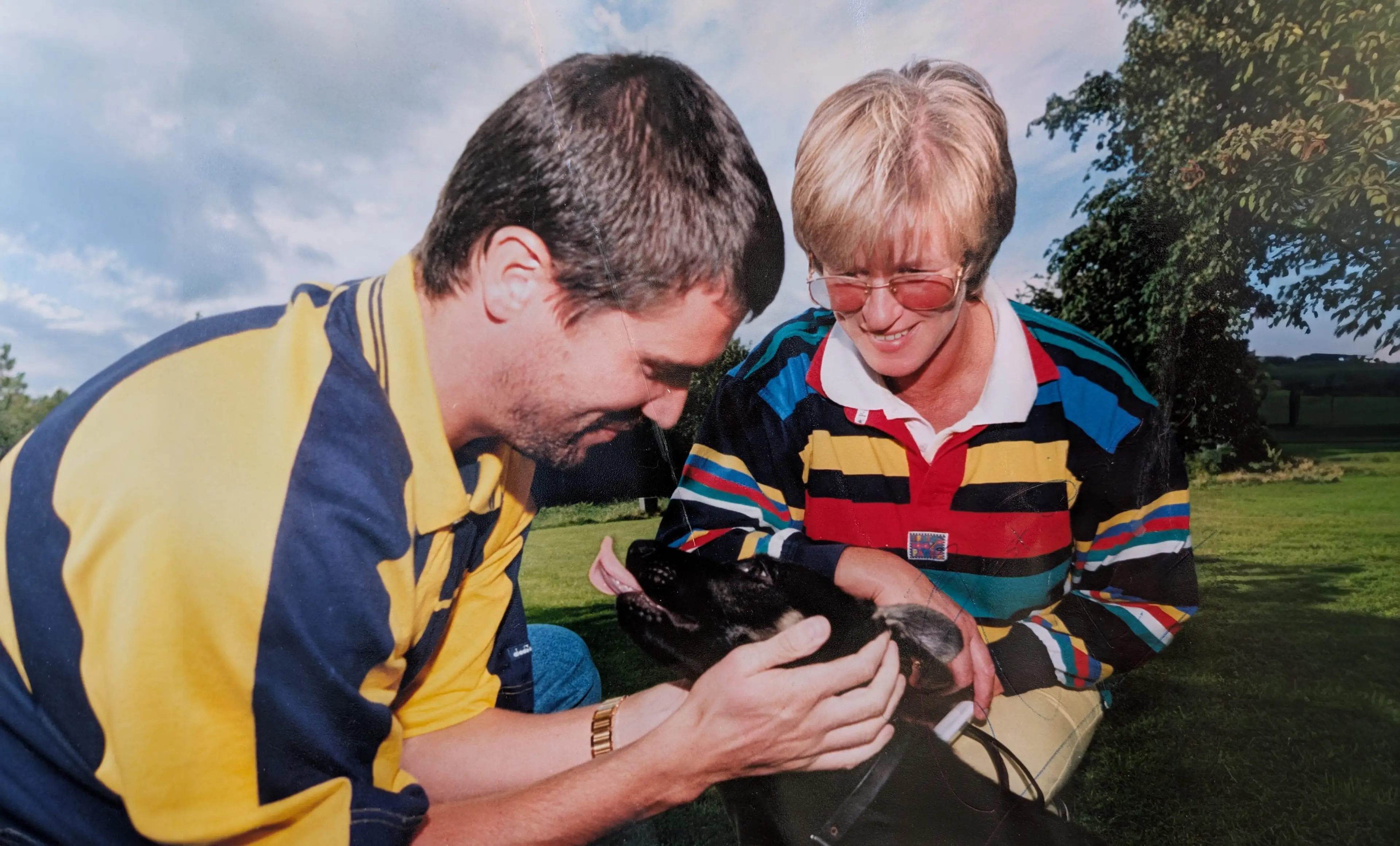 Two men in rugby jerseys examine a small black animal together outdoors on a grassy field.