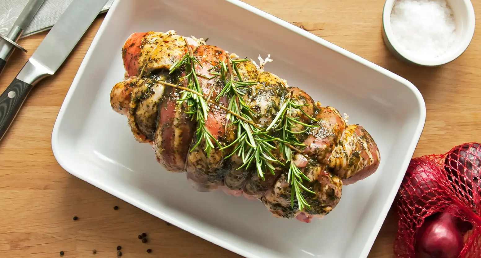 A perfectly seared beef tenderloin steak garnished with fresh rosemary sprigs is plated on a white rectangular dish, accompanied by a knife, salt, and festive holiday decorations o