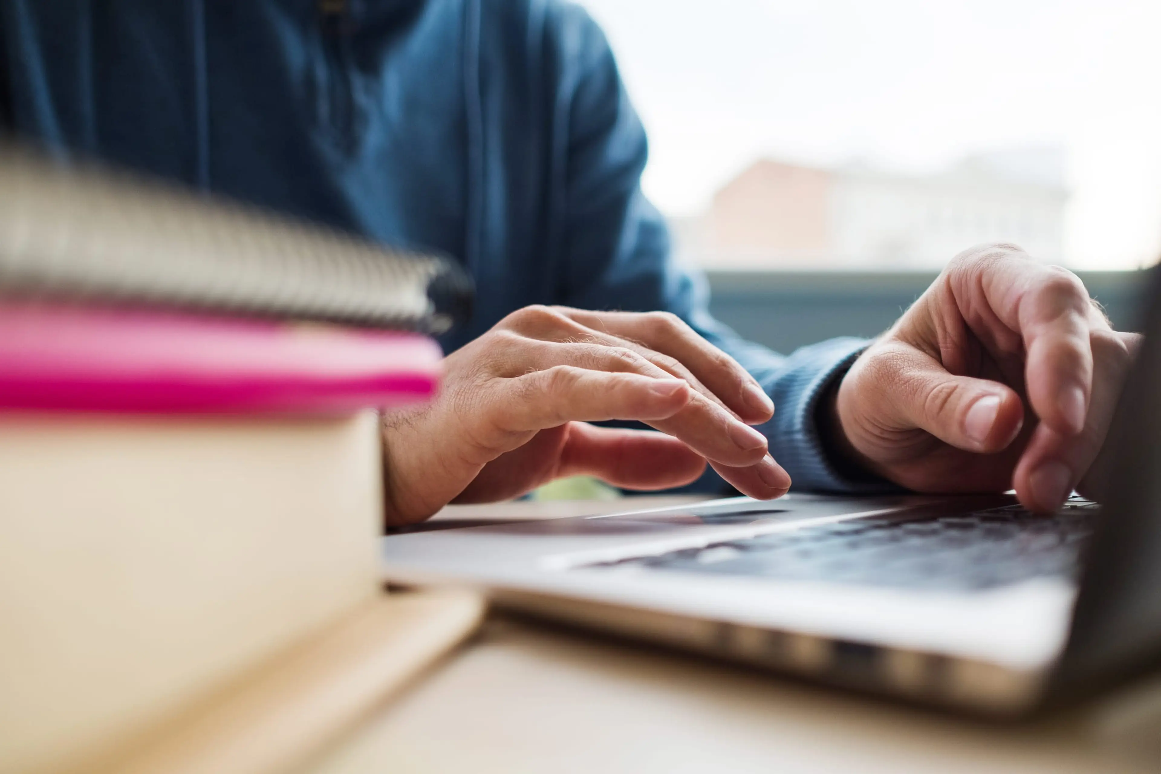 A person wearing a blue shirt points at a laptop screen while reviewing documents and color swatches on a wooden desk.