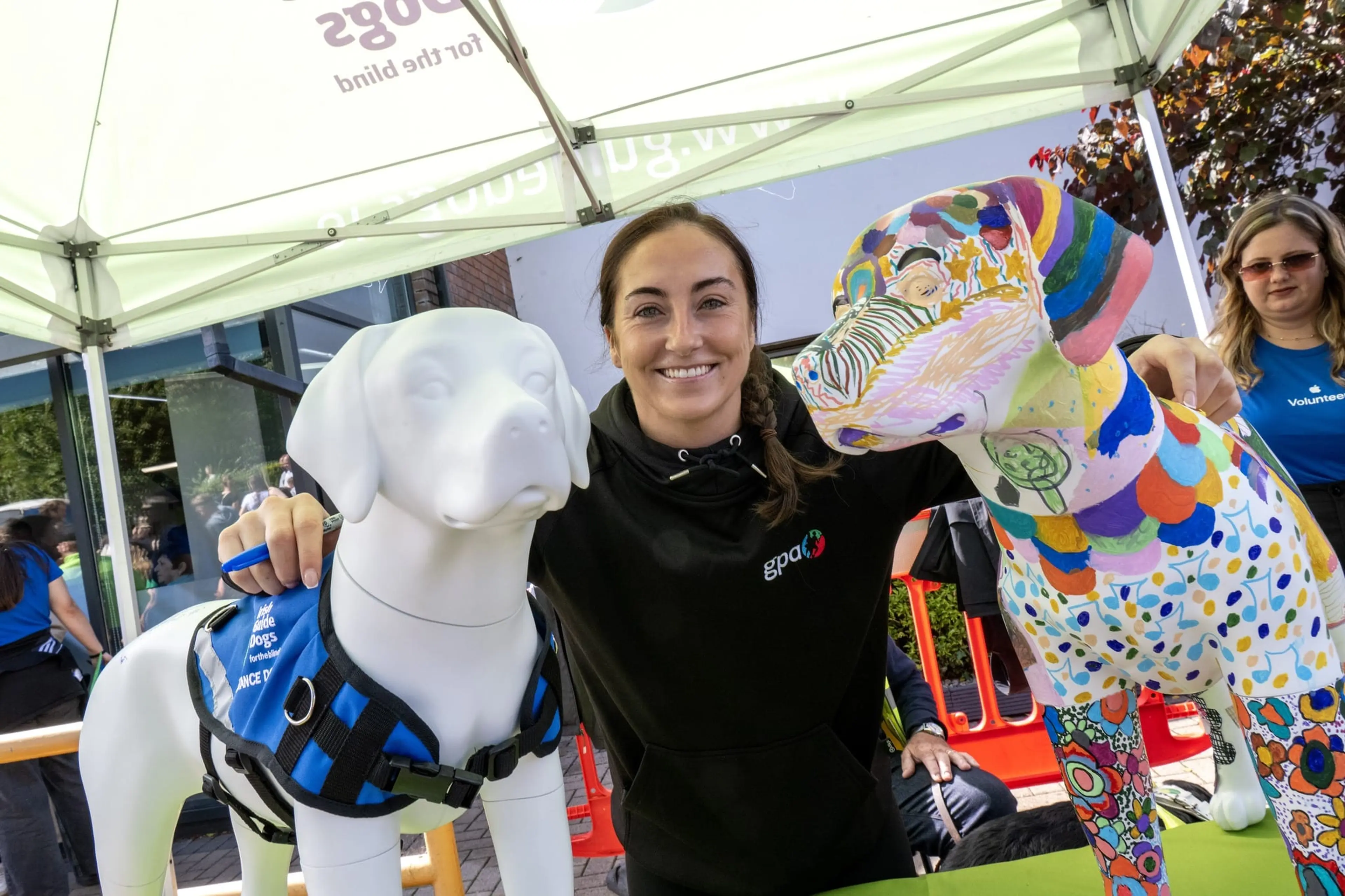 A smiling woman posing next to a colorfully painted sculpture and a white dolphin statue.