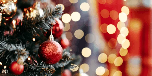 Close-up of a Christmas tree with red baubles and blurred warm lights in the background, creating a festive atmosphere.